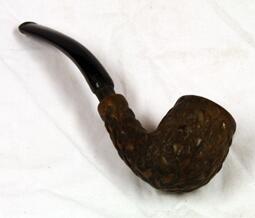 Pipe. Hode med relieffskjæringer. Bakelitt? Brun. Sort buet skaft i bakelitt. Stikkes inn i pipehodet.