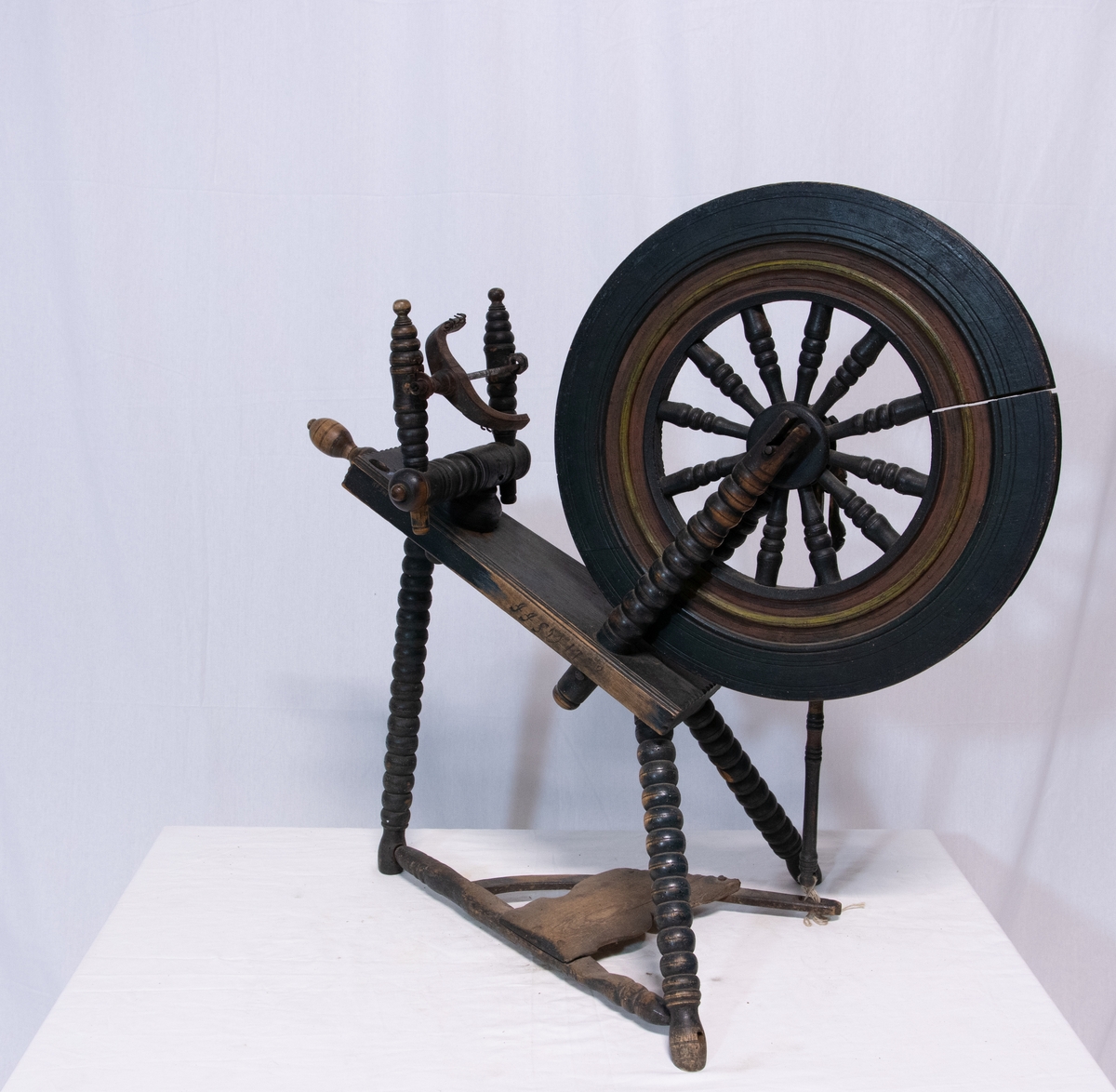 Grønnsort rokk med Trebeint skråttstillet krakk, der den ene ende er forsynt med skrue. Hjulet har tolv eker og bred rigg som henger med to skråstøtter. Forbindelse mellom hjul og pedal mangler.