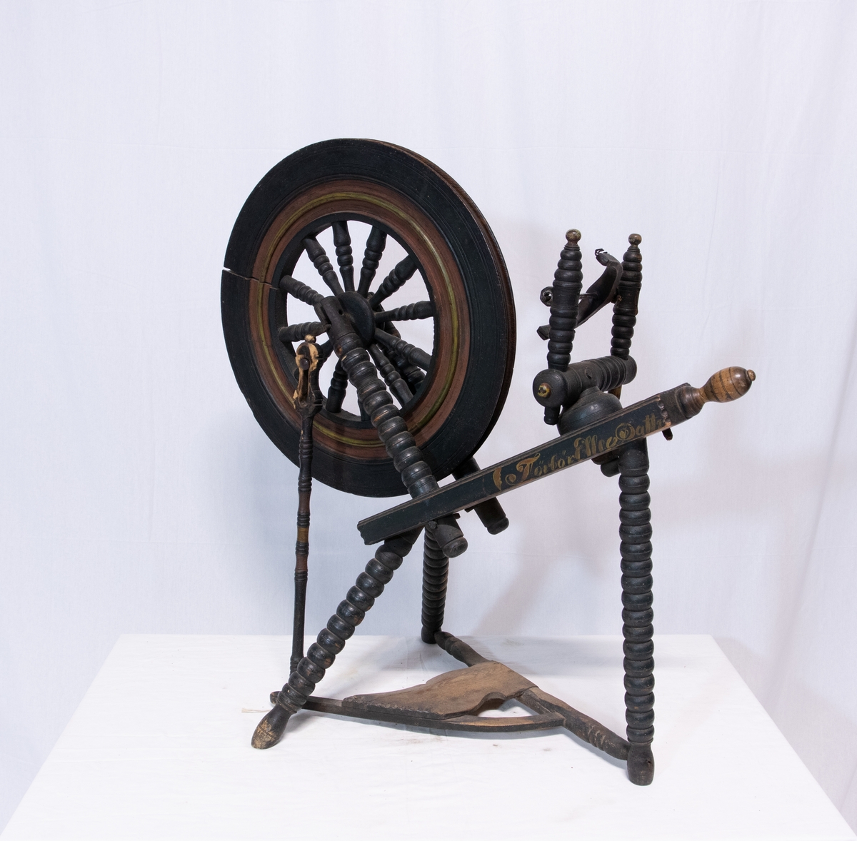 Grønnsort rokk med Trebeint skråttstillet krakk, der den ene ende er forsynt med skrue. Hjulet har tolv eker og bred rigg som henger med to skråstøtter. Forbindelse mellom hjul og pedal mangler.