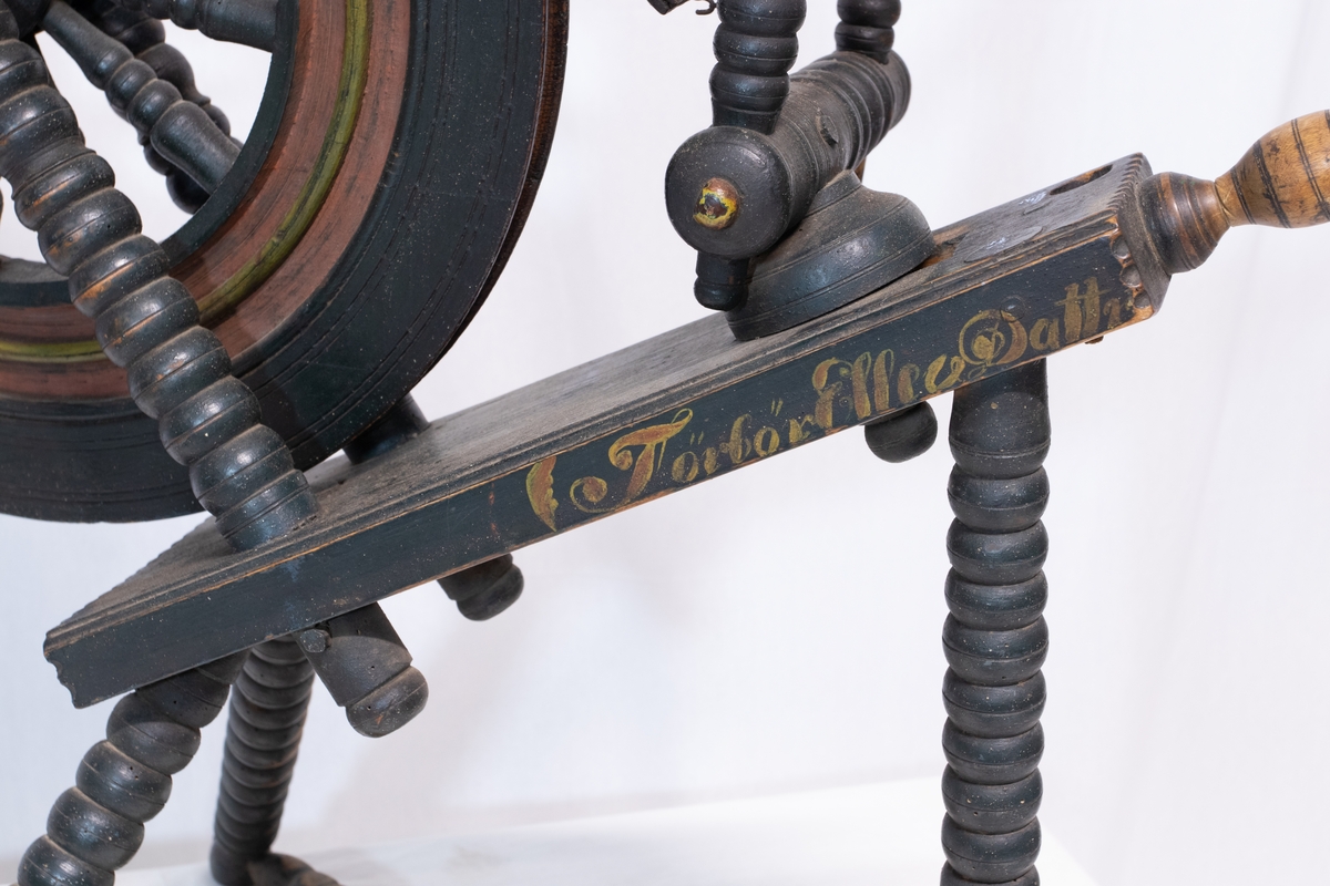 Grønnsort rokk med Trebeint skråttstillet krakk, der den ene ende er forsynt med skrue. Hjulet har tolv eker og bred rigg som henger med to skråstøtter. Forbindelse mellom hjul og pedal mangler.