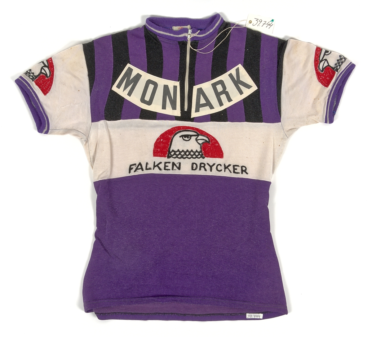 Cykeltröja i vit och lila syntet märkt: "MONARK". Tre fickor på ryggen, märkt: "MONARK" och "FALKEN DRYCKER" på både fram- och baksida. Även "Falkens" logotype på ärmarna.
Med tillhörande monarkkeps och en handske i bakfickor på tröjan.