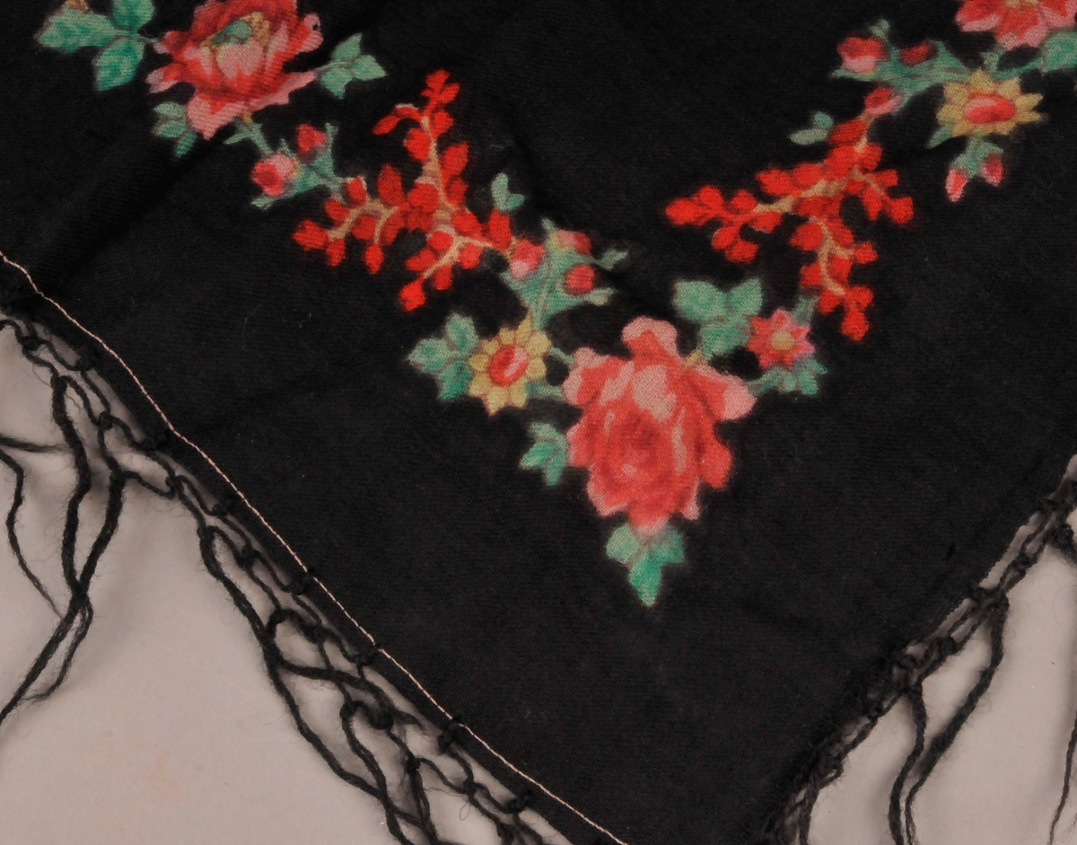 Trekanta tørkle i tynn, svart ull. Tørkledet har trykkt blomstermotiv i friske fargar.Frynser på to av sidene.