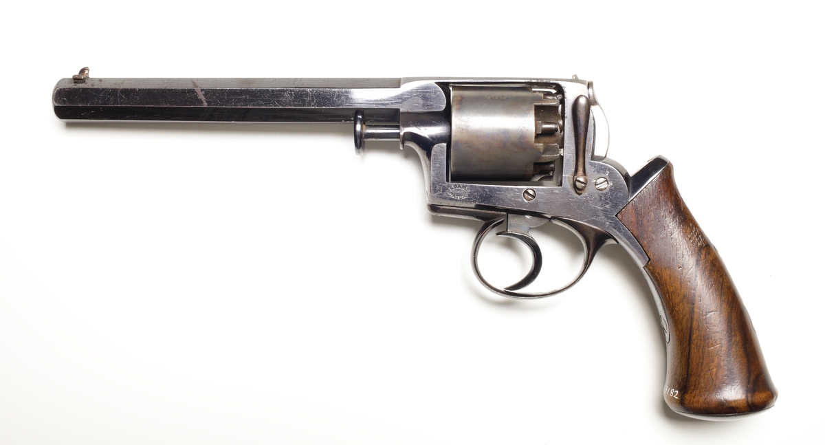 Revolver av slaglåsmodell. Den roterande trumman innehåller plats för fem laddningar. Laddning sker genom att ta loss trumman från stommen. Framför trumman sitter en spärr som trycks in, och sedan kan trumaxeln dras fram och trumman tas ur. En enkel säkring finns vid hanen som aktiveras genom att man trycker löst på avtryckaren, och samtidigt trycks säkringen in så slagstiftet inte kommer åt tändhatten. Avfyrning kan ske endast genom att trycka på avtryckaren, detta då upphakning av hanen ej är möjlig. Hela revolvern är tillverkad av blånerat stål, förutom hanen som är oblånerad. Kolvplattorna är tillverkade av mörkt ädelträ. Stomme och pipa är polerade. På kolvryggen sitter en tumplåt i silver, samt på kolvknappen en liten lucka för tändhattsförvaring. Hela vapnet är odekorerat, och pipan är åttakantig och invändigt räfflad i kaliber .54. Stomme och trumma ej nummerriktiga.
Inskrivet i huvudkatalogen 1990.