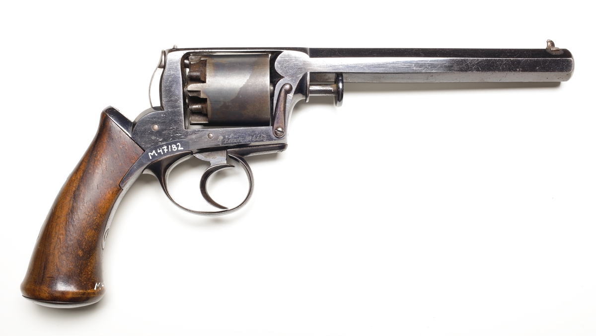 Revolver av slaglåsmodell. Den roterande trumman innehåller plats för fem laddningar. Laddning sker genom att ta loss trumman från stommen. Framför trumman sitter en spärr som trycks in, och sedan kan trumaxeln dras fram och trumman tas ur. En enkel säkring finns vid hanen som aktiveras genom att man trycker löst på avtryckaren, och samtidigt trycks säkringen in så slagstiftet inte kommer åt tändhatten. Avfyrning kan ske endast genom att trycka på avtryckaren, detta då upphakning av hanen ej är möjlig. Hela revolvern är tillverkad av blånerat stål, förutom hanen som är oblånerad. Kolvplattorna är tillverkade av mörkt ädelträ. Stomme och pipa är polerade. På kolvryggen sitter en tumplåt i silver, samt på kolvknappen en liten lucka för tändhattsförvaring. Hela vapnet är odekorerat, och pipan är åttakantig och invändigt räfflad i kaliber .54. Stomme och trumma ej nummerriktiga.
Inskrivet i huvudkatalogen 1990.