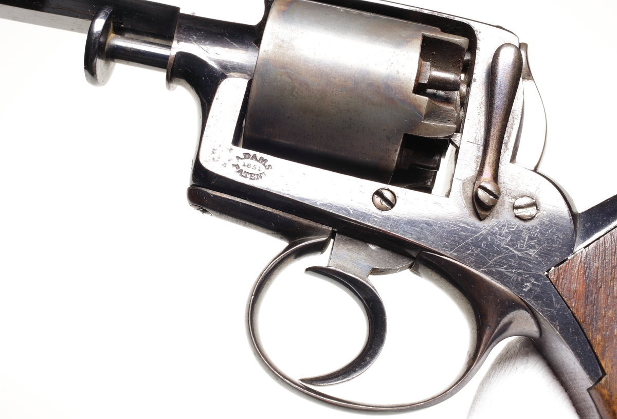 Revolver av slaglåsmodell. Den roterande trumman innehåller plats för fem laddningar. Laddning sker genom att ta loss trumman från stommen. Framför trumman sitter en spärr som trycks in, och sedan kan trumaxeln dras fram och trumman tas ur. En enkel säkring finns vid hanen som aktiveras genom att man trycker löst på avtryckaren, och samtidigt trycks säkringen in så slagstiftet inte kommer åt tändhatten. Avfyrning kan ske endast genom att trycka på avtryckaren, detta då upphakning av hanen ej är möjlig. Hela revolvern är tillverkad av blånerat stål, förutom hanen som är oblånerad. Kolvplattorna är tillverkade av mörkt ädelträ. Stomme och pipa är polerade. På kolvryggen sitter en tumplåt i silver, samt på kolvknappen en liten lucka för tändhattsförvaring. Hela vapnet är odekorerat, och pipan är åttakantig och invändigt räfflad i kaliber .54. Stomme och trumma ej nummerriktiga.
Inskrivet i huvudkatalogen 1990.