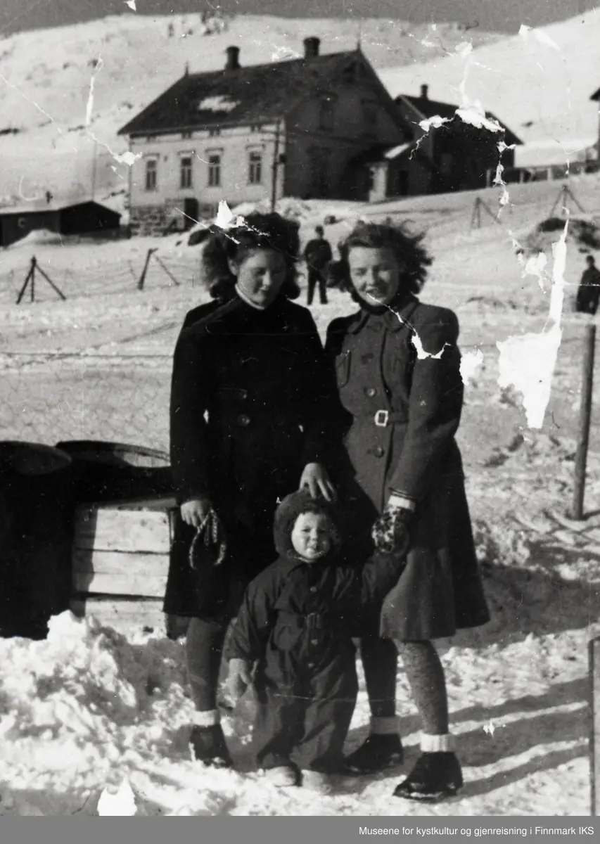 Honningsvåg. Gruppebilde av to unge damer og et barn. I bakgrunnen ser man Prestegården. Begynnelsen av 1944.