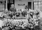 Man omgiven av blomsterarrangemang.
Fotografens ant: Maskininspektör Olsson 18/7 1936.