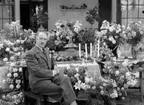 Man omgiven av blomsterarrangemang.
Fotografens ant: Maskininspektör Olsson 18/7 1936.