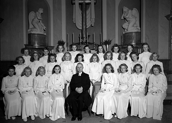 Konfirmander, samt Pastor Holm i Karlstad Domkyrka.
Under 400 år låg stadens kyrka där Stadshotellet nu ligger. Denna kyrka brann ner 1719 och en ny byggdes på Lagberget. Denna uppfördes av byggmästare Christian Haller från Sachsen och kunde invigas den 2 juli 1730. Ett kupoltorn byggdes till 1737. När nästan hela Karlstad brann 1865 drabbades också domkyrkan. Kyrkklockorna störtade ner och tornspiran föll på kyrktaket. Detta fattade eld och rasade in. Vid återuppbyggnaden fick Kyrktornet sin nuvarande form.
Domkyrkan har renoverats senast 1998.
Källa: Karlstads fasader, Anita Meyer-Lie, Per Berggrén. Tryckår 1999.