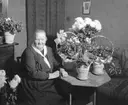 Kvinna sitter vid bord med blomsterarrangemang.
Fotografens ant: Herr Kihlberg 14/12 1935.