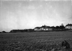 Åker i förgrunden och större hus i bakgrunden, institutionsb