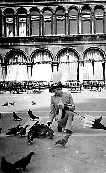 Dam med hatt och paraply matar duvor.