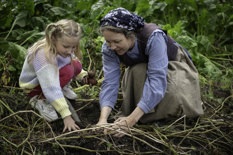 En jente og en dame tar opp poteter.