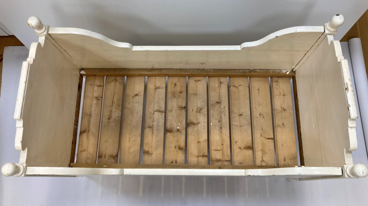 Rektangulær, hjemmelaget barneseng av furu. Sengekassen er tappet inn i sengestolpene med brede tapper, og er bygd av planker. Langsidene består av en planke med en formet sengekarm tappet i hver ende. Kortsidene består av to planker som er tappet sammen i høyden, der den øverste planken er formet. En liten list er tappet på toppen av kortsidene. Fire sengestolper, hver med en dreiet knapp på toppen, og dreide ben. Sengebunn av ti bord av ubehandlet furu, festet til to lekter med spiker langs sengens langside. Det ene benet er forlenget sekundært med gummiknott spikret opp i benet. Sengen er malt tre ganger, først i grønn, så i gult så i eggeskallhvitt. 