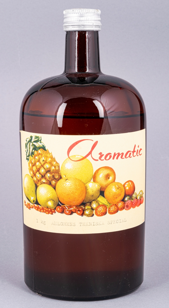 Glasflaska, brun, med skruvkork. Innehåller essens. Etikett: "Aromatic 1 kg Ahlgrens Tekniska special" samt frukter.