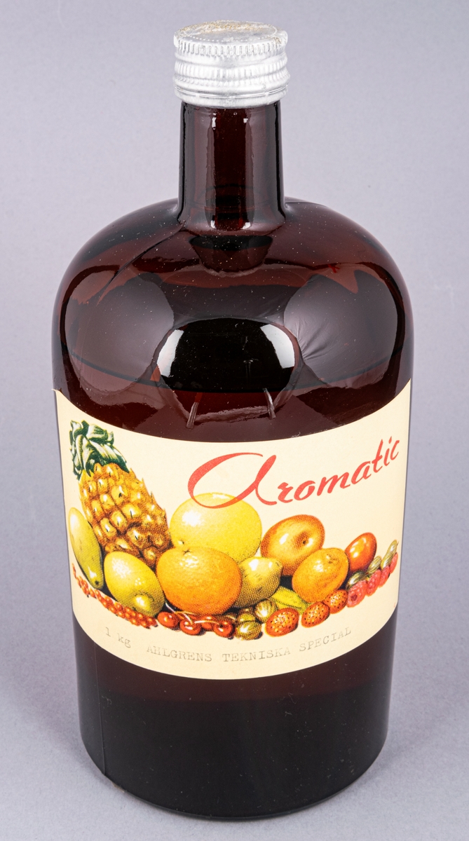 Glasflaska, brun, med skruvkork. Innehåller essens. Etikett: "Aromatic 1 kg Ahlgrens Tekniska special" samt frukter.