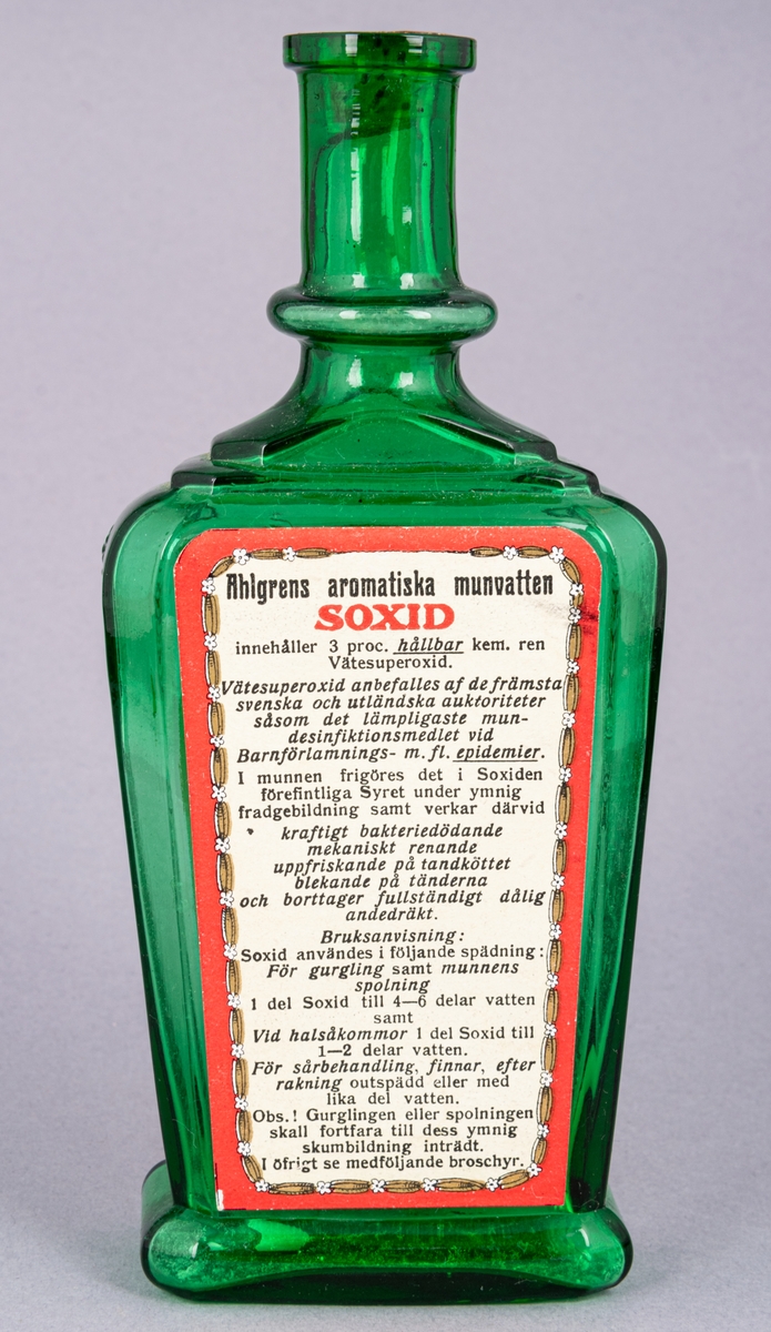 Glasflaska för munvatten, grön, rektangular, med kork. Profilerad skuldra. Etiketter på fram- och baksida. Präglad text på sidorna.