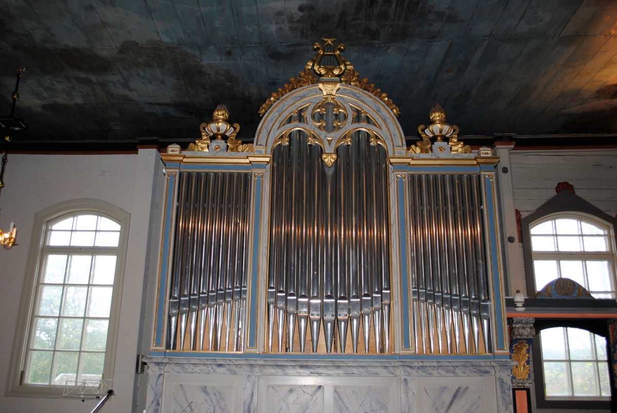 Interiör i Laxarby kyrka. Altaruppsatsen är från 1769 och centralmotivet består av en så kallad kalvariegrupp med Kristus på korset omgiven av Maria och aposteln Johannes. Uppsatsen, liksom predikstolen från 1747, två änglar med psalmnummertavlor från 1767, och en timglasängel, är alla utförda av den i stiftet välkände bildsnidaren Isak Schullström. Taket dekorerades 1777 med moln och stjärnor av kyrkomålaren Carl Zetterström.