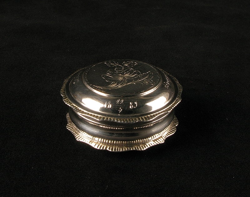 Svampdosa av silver med ingraverad blomma på locket.