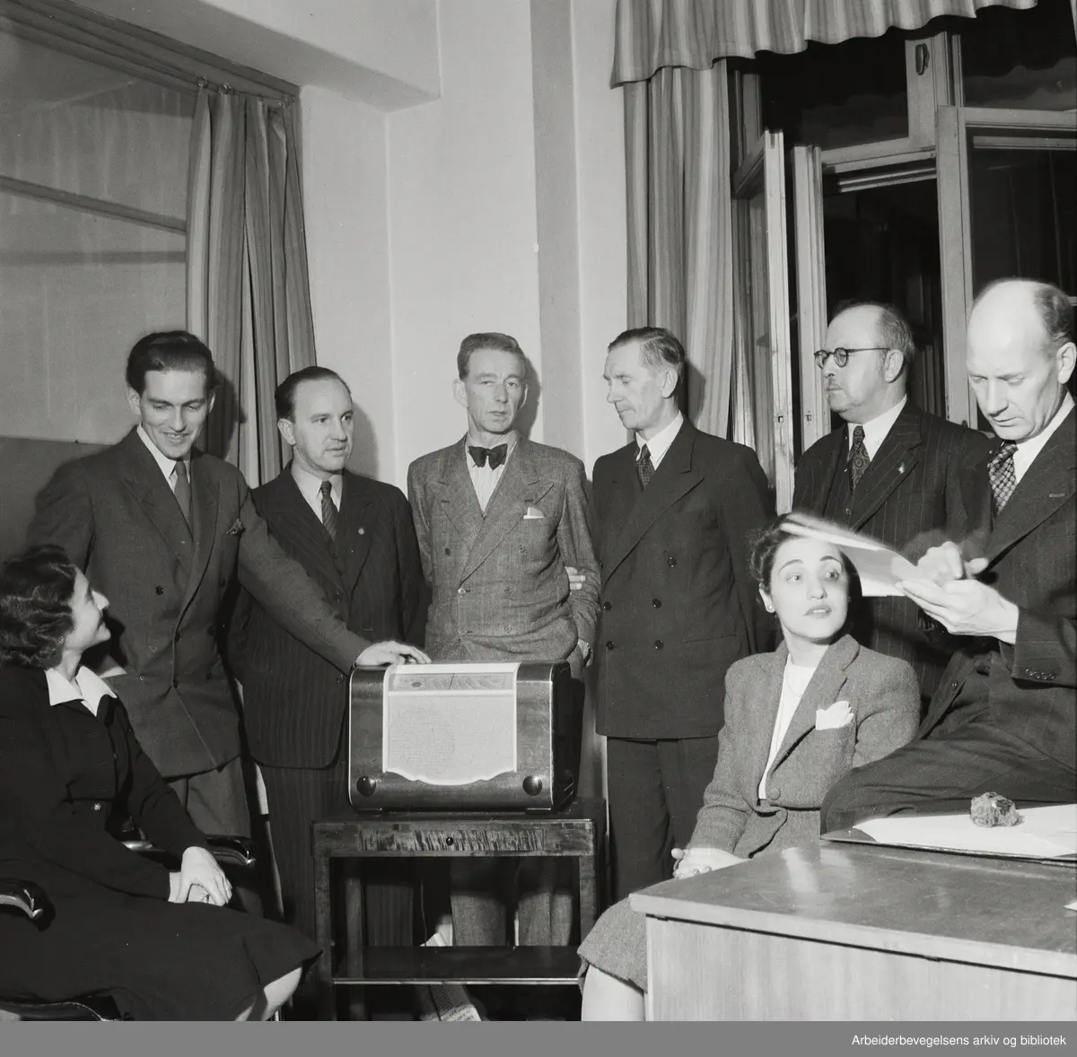 Stortingsvalget 1945. Besøk i Arbeiderbladets redaksjon på valgnatta. Fra v.: Fru Galenson fra USAs ambassade i Oslo, Arne Björnberg og Herberth Yve fra Stockholm, Lars Evensen, Oscar Torp, Ernst Christiansen fra Socialdemokraten i København, Miriam Sluchin fra USAs ambassade i Oslo og Einar Gerhardsen.