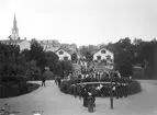 Uppklätt och förväntansfullt i Linköping när staden fick besök av kung Oscar II sommaren 1893. På vägen från järnvägsstationen mot slottet stannade konungen till i Trädgårdsföreningen för en promenad genom parkens lummiga gångar. Fotograf Sohlberg stod i ett fönster till restaurangen och frös ögonblicket kort före händelsen.