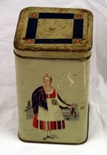Boks. Metall. 4-sidet med kvadratisk bunn og topp. Påhengslet lokk. Beigemalt med bunadkledt dame på hver langside. Geometrisk ornamentikk på lokket. Blank metall innvendig.
