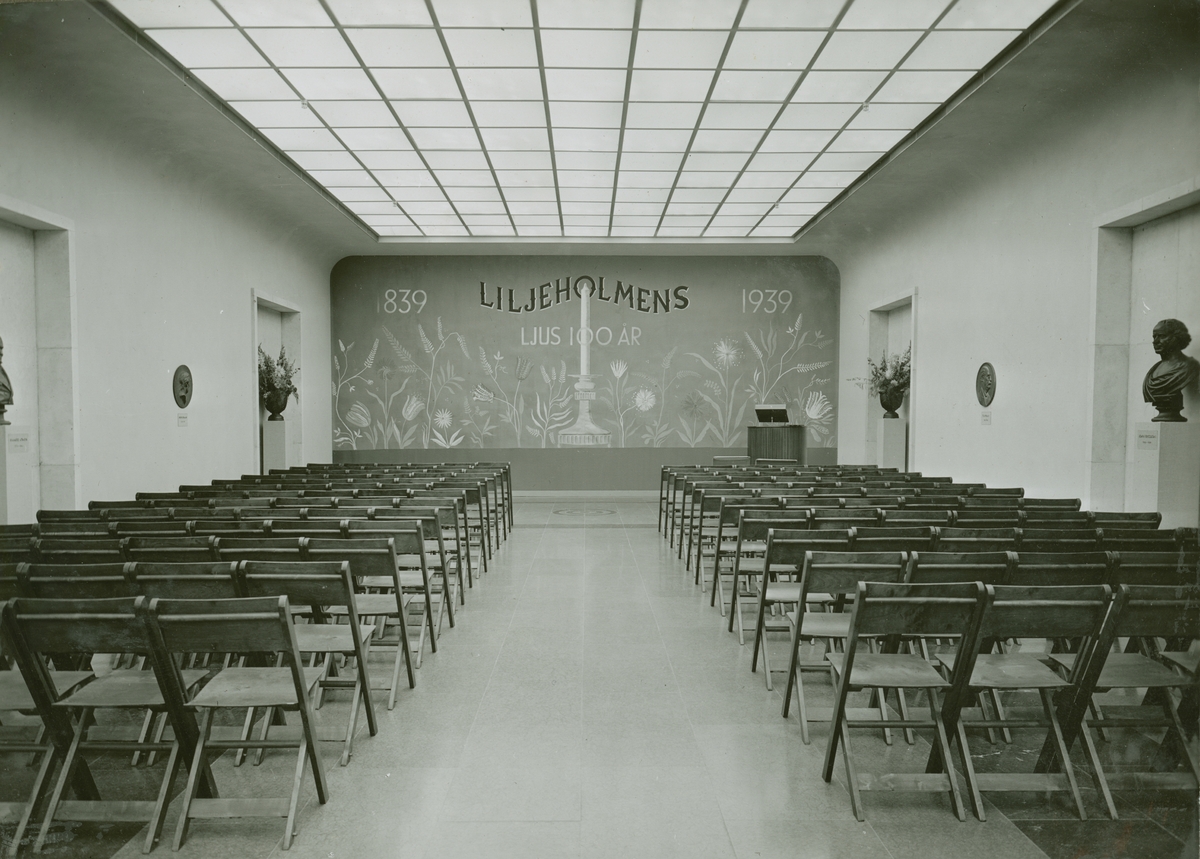 Tekniska museet, ca 1939. Sverigesalen, möblerad som föreläsningssal. Fonden dekormålad med ett stort ljus och texten "Liljeholmens ljus 100 år, 1839 - 1939". Foto mot söder.