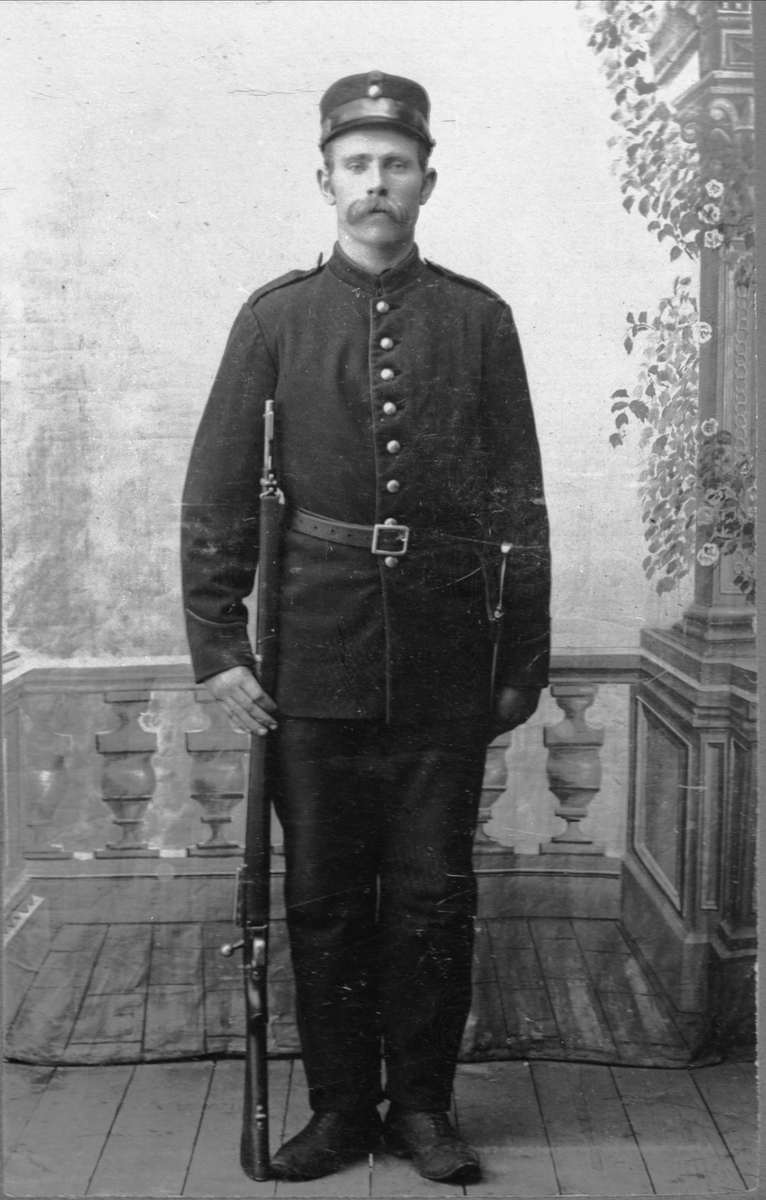 Studioportrett av mann i militær uniform med gevær.