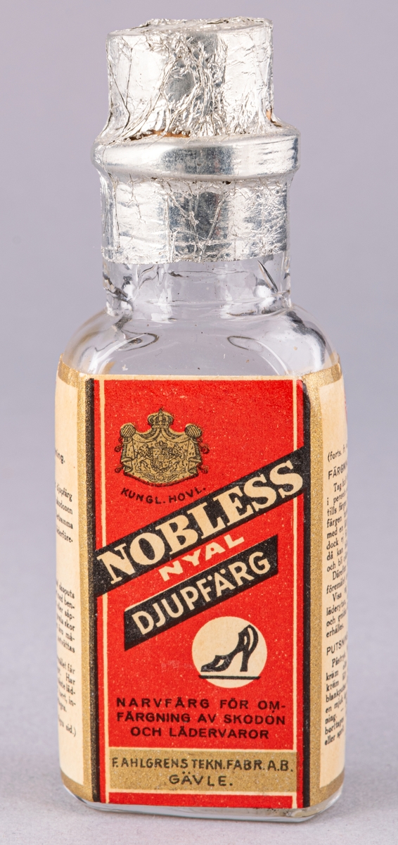 Rektangulär glasflaska för skofärg, med kork. Röd etikett med tryck i svart och vitt. Bruksanvisning på sidan.