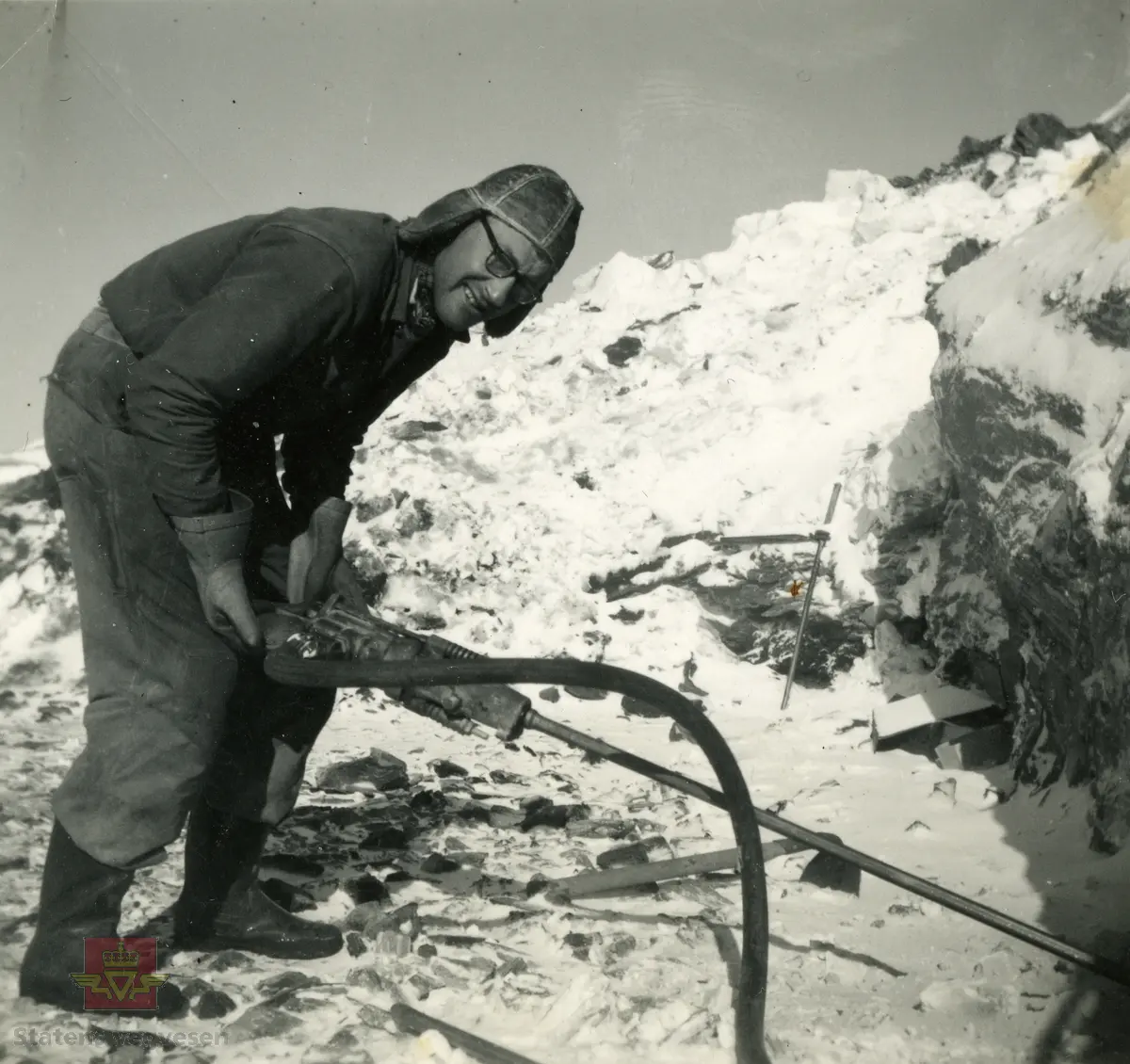 Sverre Sandstrand i arbeid med bruk av borhammer.
Bilde er tatt i mars 1958 på FV 104 på Sørøya i Finnmark.