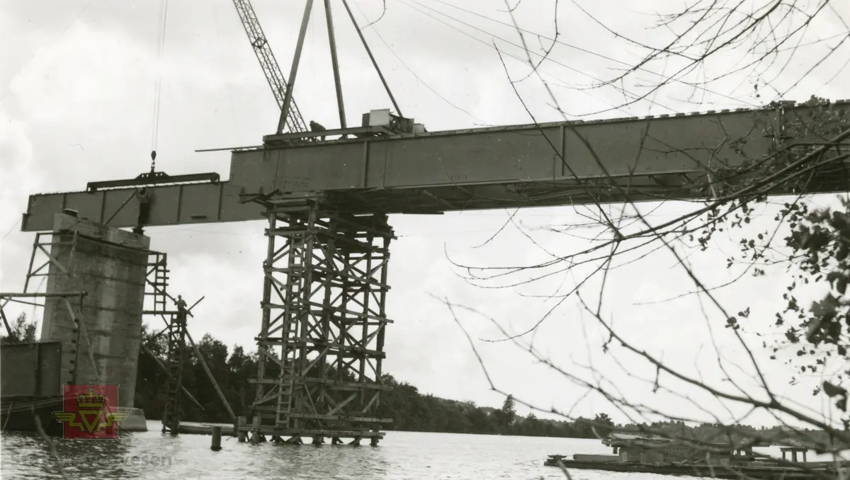 Gamle Minnesund bru. Heising av dragere for montering på betongfundament. 
Legg merke til tre menn som arbeider uten noen form for sikring på brua.
Ref. til artikkel om Minnesund bru i "Store norske leksikon." 
Ref. til Nr. 87-90 Minnesund vegmiljø i  "Nasjonal verneplan for veger, bruer og vegrelaterte kulturminner. Statens vegvesen - Region Øst"