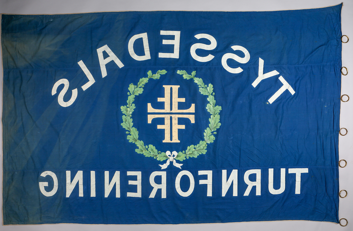 Motiver er sett saman av to eikegreiner bundne saman med ei sløyfe og Turnforbundet sitt symbol/logo, 4 F-ar, i midten.