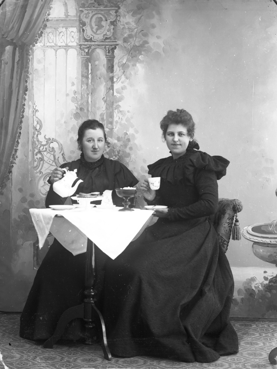 Atelierfoto.To kvinner sitter ved et bord og drikker kafe/te.
Skrevet på papir som er festet til negativet: 605. Marie Østbye.
"Marie Østbye" er vel sannsynligvis gårdmannskone Marie Østby på Søndre Byveien på Østre Toten f. 1878, Østre Toten. Folketelling 1900: https://www.digitalarkivet.no/pf01037091004897
