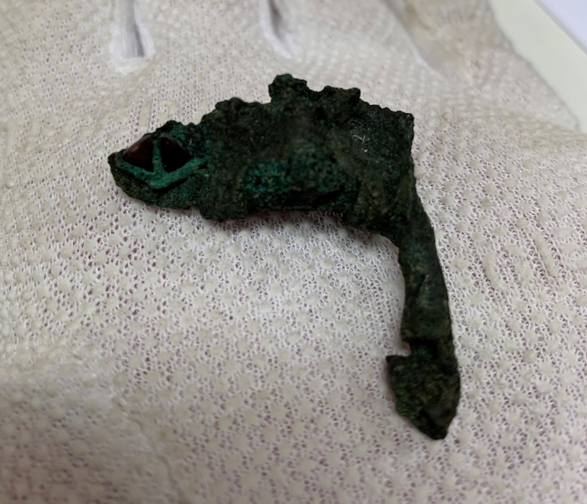 Föremål av kopparlegering. Sölja eller möjligen en remlöpare. Prydd med granater. Fragment.