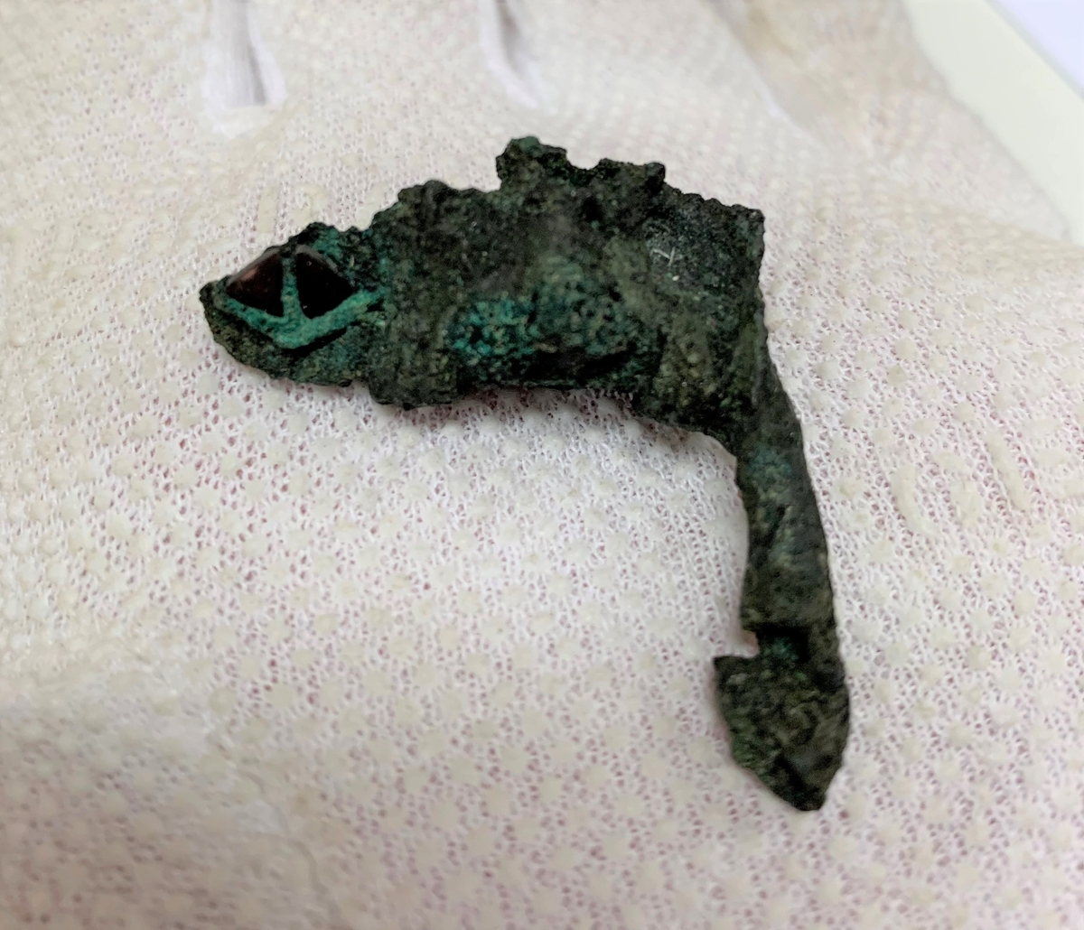 Föremål av kopparlegering. Sölja eller möjligen en remlöpare. Prydd med granater. Fragment.