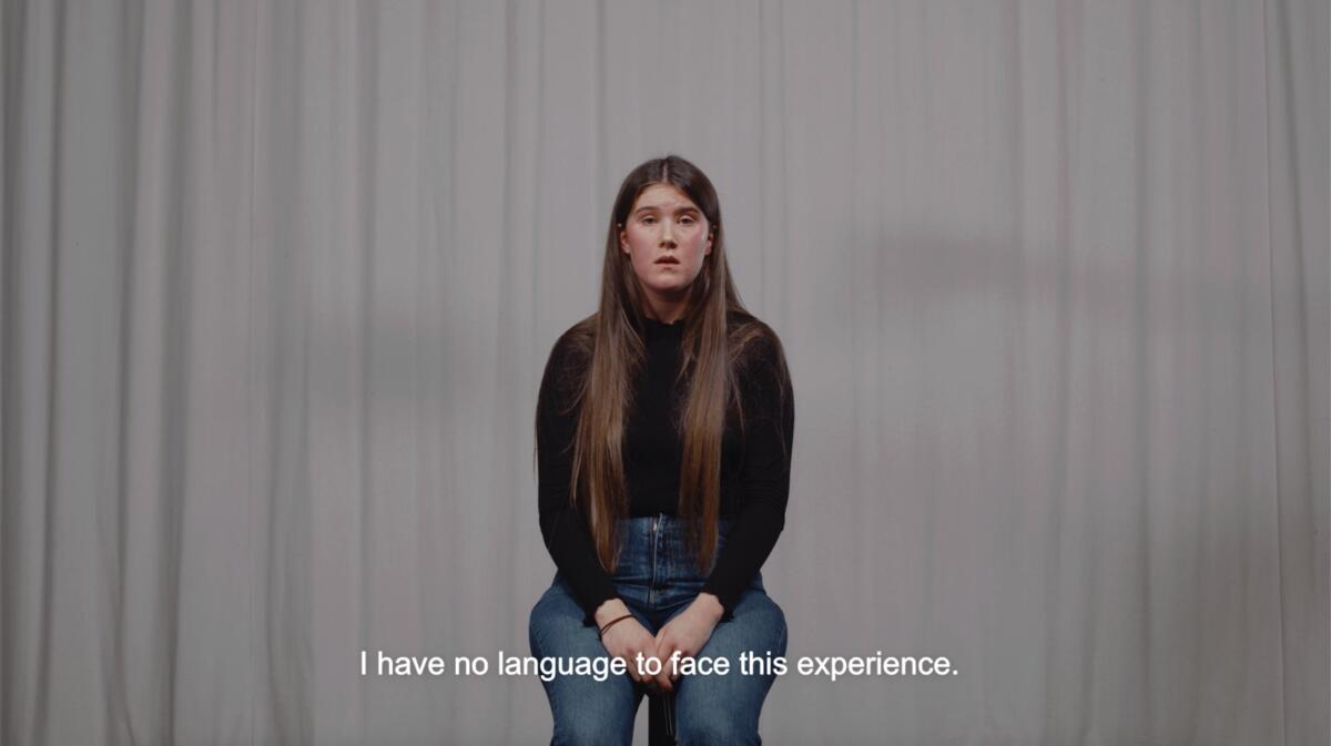 Bilde av en person med langt hår, sitter foran et sceneteppe. 