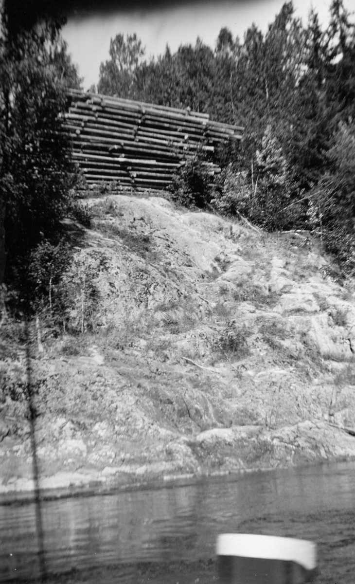 Tømmertillegging i berglendt terreng, sannsynligvis i nærheten av Fossumbogen ved Glomma i Spydeberg. Fotografiet skal være fra 1933. Det er tatt fra vannet, mot en nesten vegetasjonsløs bergskråning. På flata på toppen av denne bergskråningen lå det ei diger strøvelte. Slike velter besto av et antall floer - lag med paralleltliggende tømmerstokker, plassert vinkelrett på såkalte strøstokker, som det her var tre av mellom hver flo. Strøstokkene skulle åpne for lufting, slik at tømmeret fikk en forsiktig tørk før de ble slått på vannet. Her var det minst 16-17 floer. Ettersom stokkene i floene lå parallelt med elvebredden og vassdragets flytretning, var det bare å rulle dem utfor når vannføringa i elva høvde for fløting.