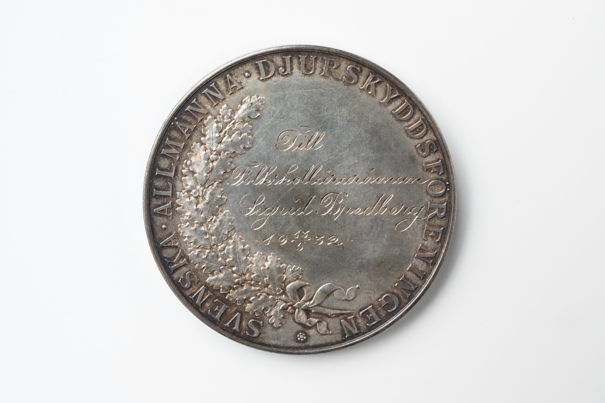 Medalj av silver graverad av Adolf Lindberg. Text runt framsidan: "SVENSKA ALLMÄNNA DJURSKYDDSFÖRENINGEN", och i centrum "Till Folkskollärarinnan Sigrid Bredberg 13/5 1932" samt på vänster sida bild av trädgren med ekblad. Text runt baksidan:" OSCAR II SVERIGES GÖT O VEND KONUNG", och i centrum profilbild av Oscar II.

Till medaljen hör en svart ask klädd invändigt med blått sametstyg i botten och gult sidentyg på insidan av locket.