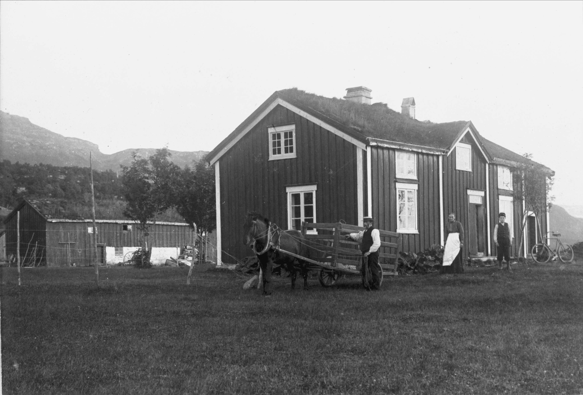Folk med hest og høyvogn på gårdstunet foran et hus på Vikeland.