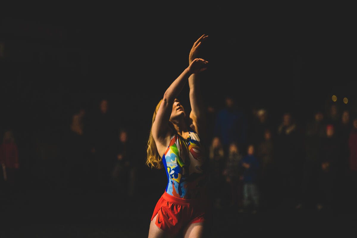 Dans på stien, foto fra tidligere arrangement, kvinne som danser. Hun har armene hevet over hodet, det er mørkt og hun belyses av en lyskilde nedenfra.