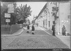 Klostergatan i hörnet mot Ågatan. Man ser diverse skyltar, hovslageri, veliocipeder samt sybehör. Man ser några människor samtala i korsningen. 

 Bilder från gatuhörn i staden Linköping åren 1909 till 1913. Bilderna är tagna i centrala Linköping i ett projekt att dokumentera Linköping för Linköpings stad.