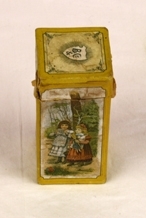 Boks. Papp. Rektangulær med kvadratisk lokk og bunn. Lokket trees på. Pålimt papir rundt boksen med skrift og illustrasjoner. Illustrasjon av 2 småpiker på en side. Gutt på motsatt side.