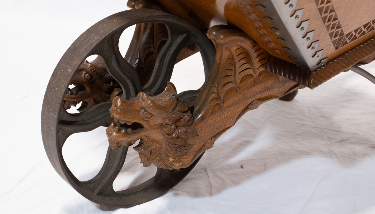 Trillebår av tre med metalhjul og detaljer. Trillebåren er dekorativt ingravert med blant annet drage detaljer.