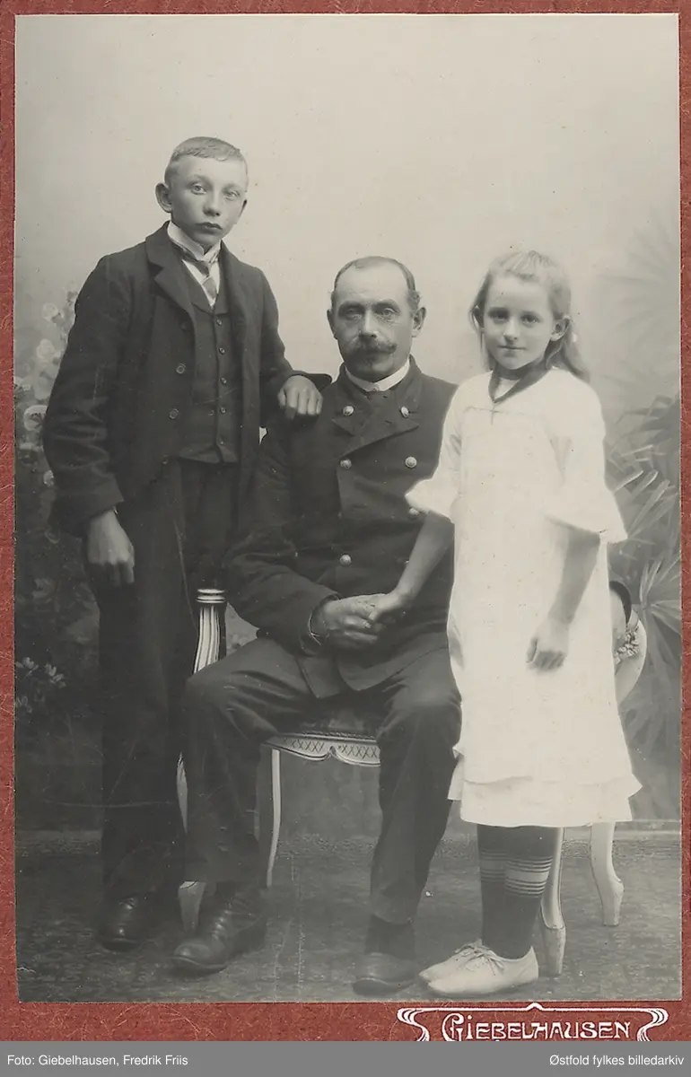 Gruppebilde av familie. Ukjent far og to barn i fotoatelier.