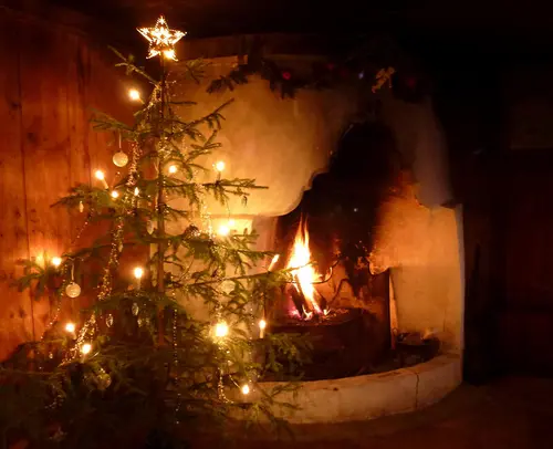 A fire is burning in an open fireplace, and a decorated Christmas tree is standing next to it.