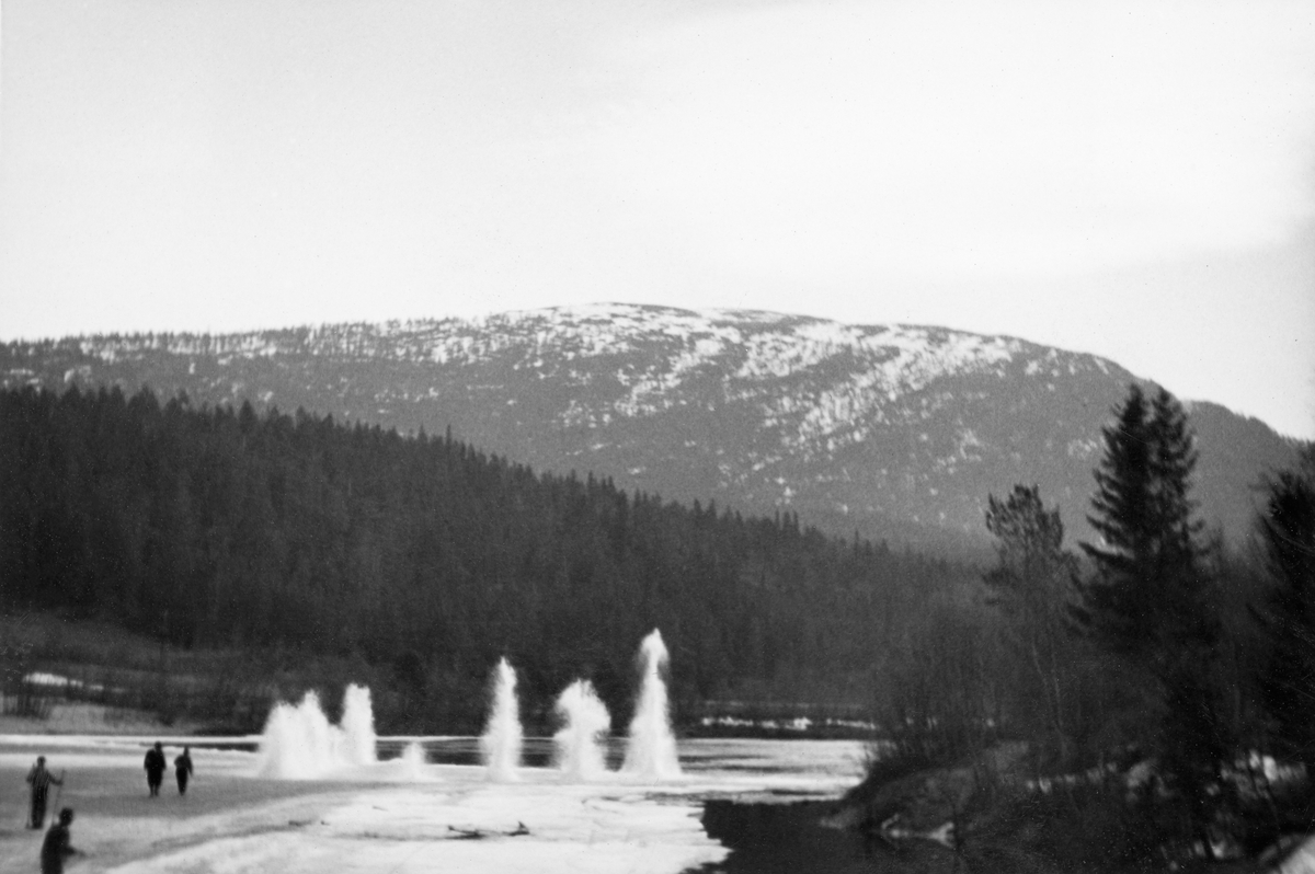 Sprening av ispropp i Glomma i nærheten av Kveberg i Alvdal 2. mai 1934. Dette ble sannsynligvis gjort for å åpne passasjer i elveløpet og forebygge at store mengder is og fløtingsvirke skulle øve for stort press på Kvebergsbrua. Dette foretaket lyktes ikke. Brua kollapset cirka fem døgn etter at dette fotografiet ble tatt. Her ser vi hvordan en serie dynamittladninger ble detonert mens fire karer observerte eksplosjonen på trygg avstand.