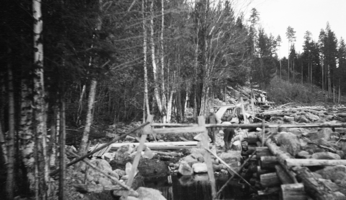 Bygging av en ny skådammen ved Båtmyrvelta i elva Søndre Osa i Åmot kommune i Hedmark høsten 1929. Fotografiet viser ei gruppe arbeidere som la opp en tørrmurt skådam i en slak yttersving. Den nye skådammen ble lagt i le av en eldre steinfylt tømmerkistekonstruksjon, som sannsynligvis skulle fjernes så snart den nye muren var ferdig. Skådammene skulle fungere som ledeskjermer for fløtingsvirket og hindre at stokkene drev inn på elvebredden. Fotografiet SJF.1990-01004 viser dammen slik den så ut året etter, med sementpusset krone og fuger på den sida som vendte mot elveløpet.