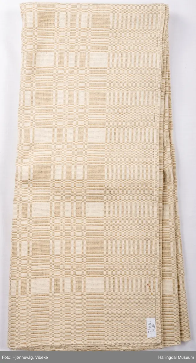 Linduk, linrenning og lin i innslag, beige. Danner ruter ig striper, tavlebragd. Duken er vevd i to lengder som er sydd sammen på midten med håndsøm.