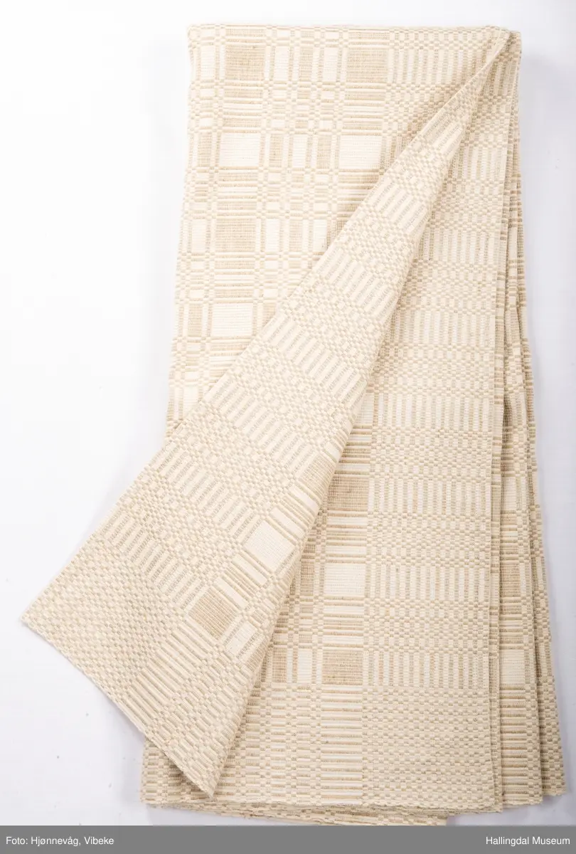 Linduk, linrenning og lin i innslag, beige. Danner ruter ig striper, tavlebragd. Duken er vevd i to lengder som er sydd sammen på midten med håndsøm.