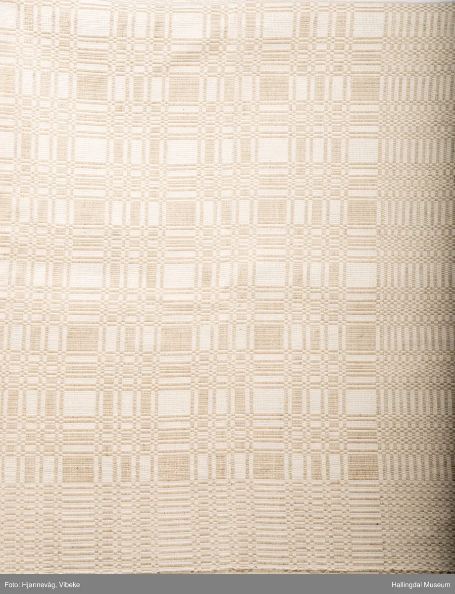 Linduk, linrenning og lin i innslag, beige. Danner ruter ig striper, tavlebragd. Duken er vevd i to lengder som er sydd sammen på midten med håndsøm.
